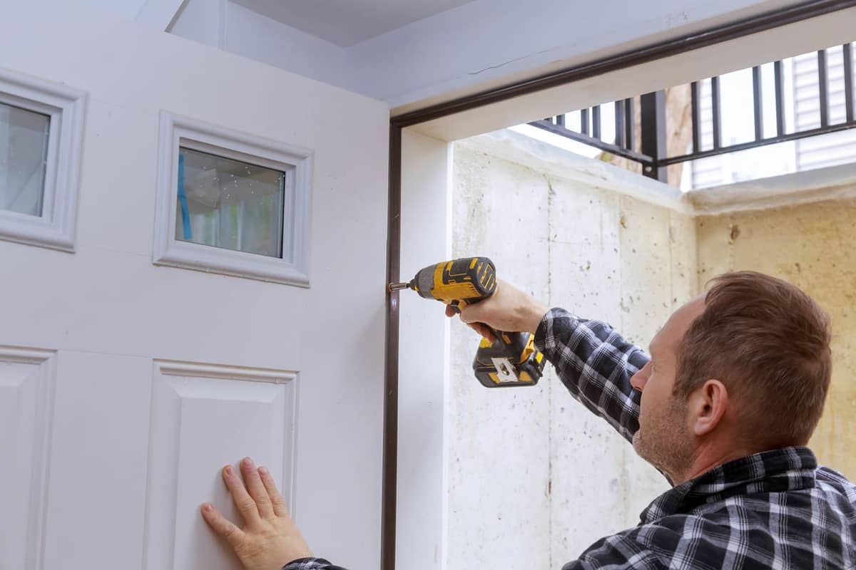 A drill driving a screw into a door hinge.